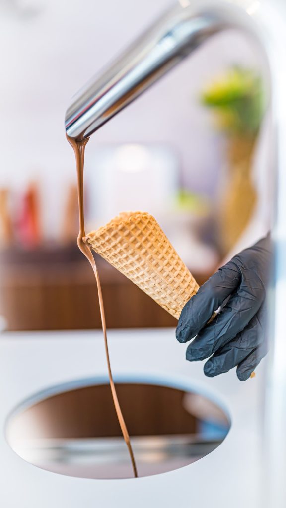 Gloved hand holding homemade waffle cone under chocolate drizzle